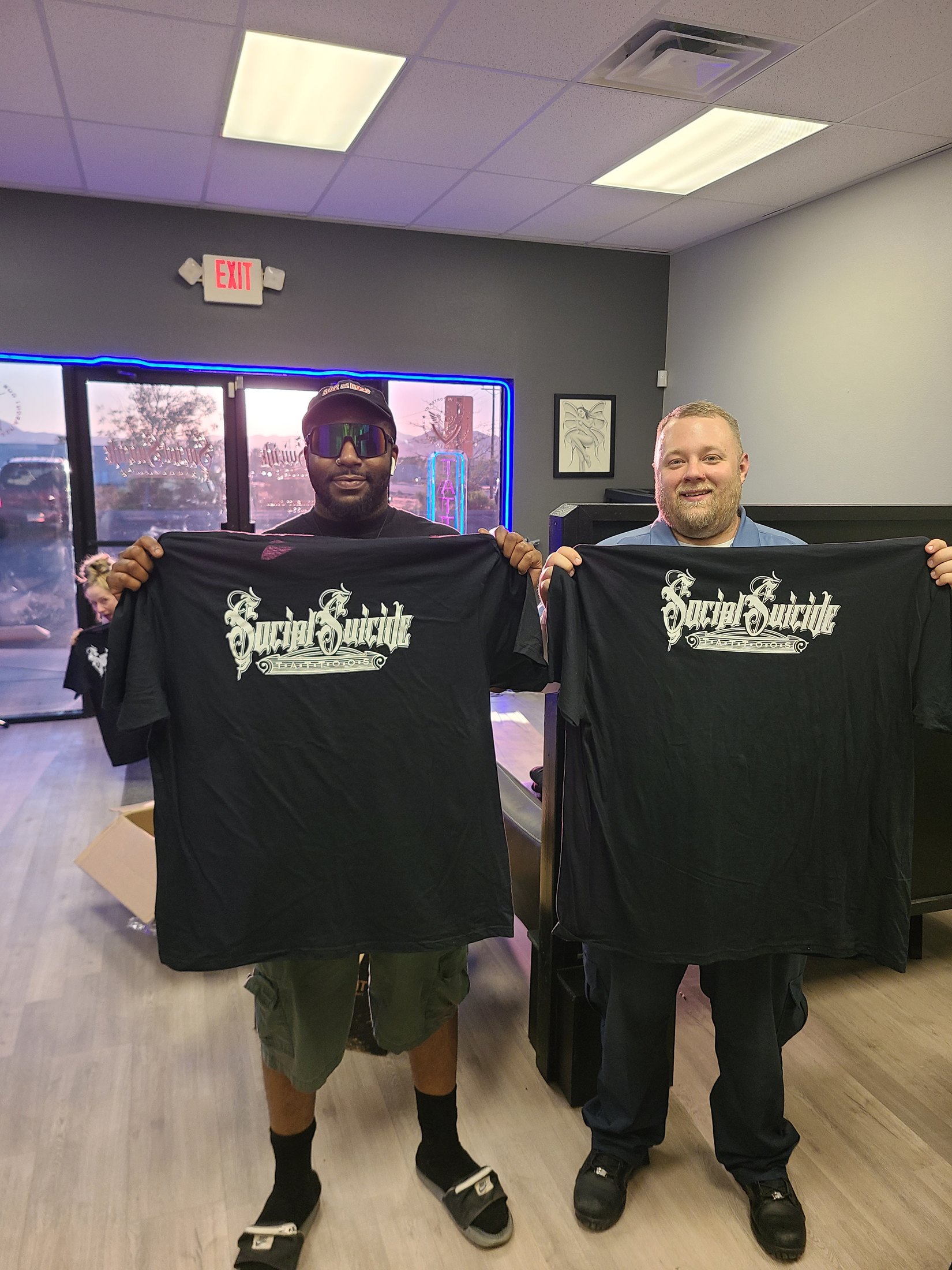 Clients holding Social Suicide Tattoos shirts inside the Pahrump tattoo shop